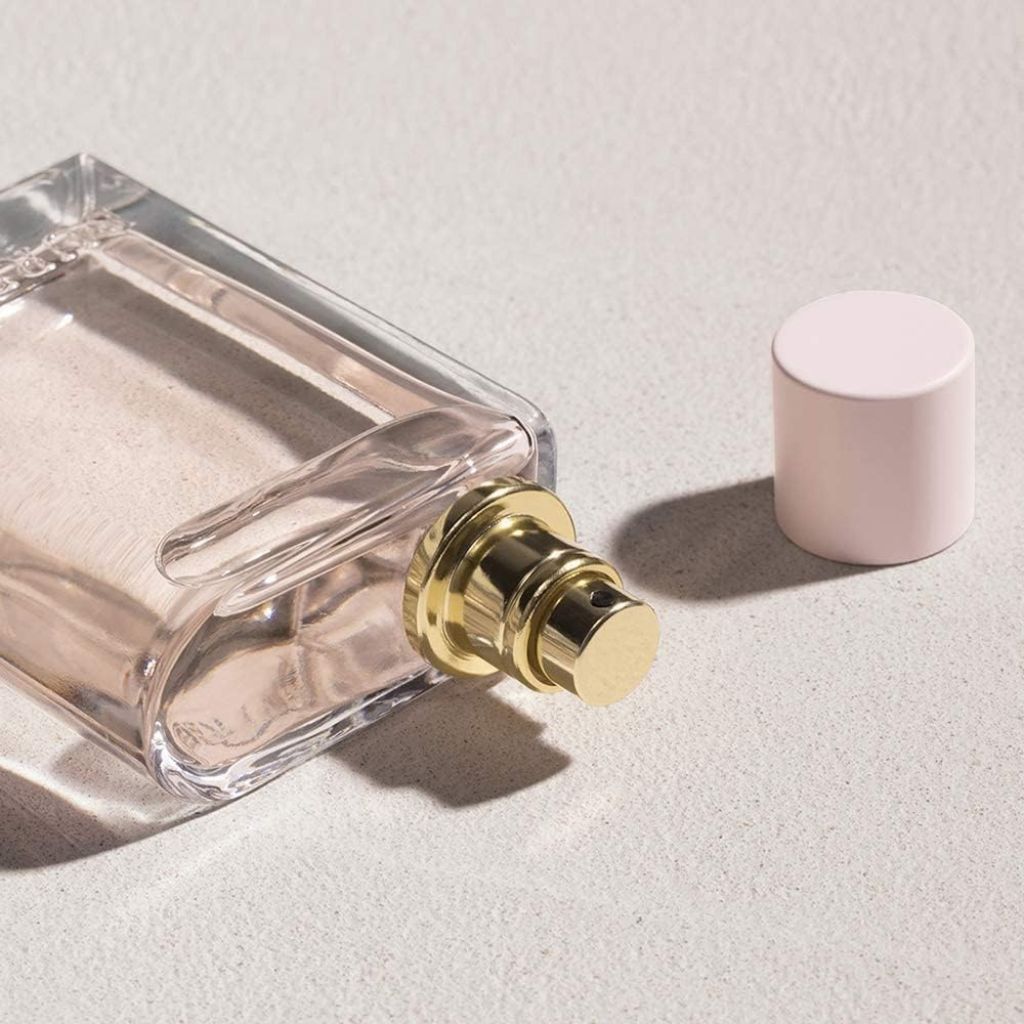 Clear perfume bottle with gold cap and pink cap on a light gray background