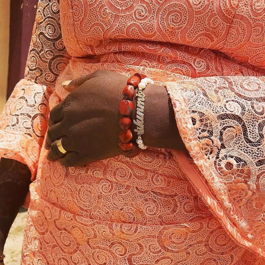 Person wearing a red and white patterned garment with a hand adorned with jewelry.