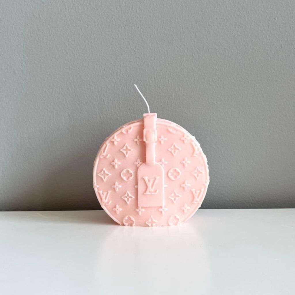 Pink round candle with a brand logo on a gray background