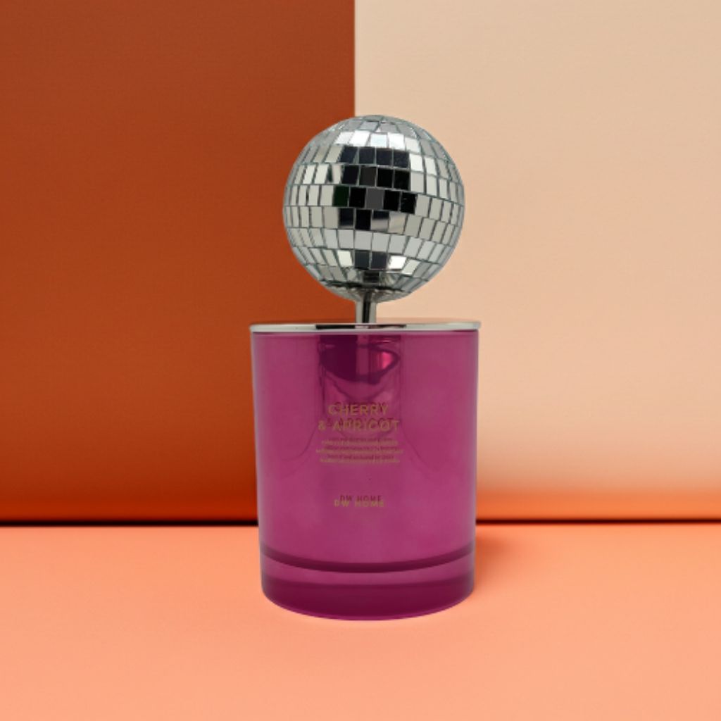Pink candle with 'Cherry & Apricot' text next to a disco ball on a pink and beige background