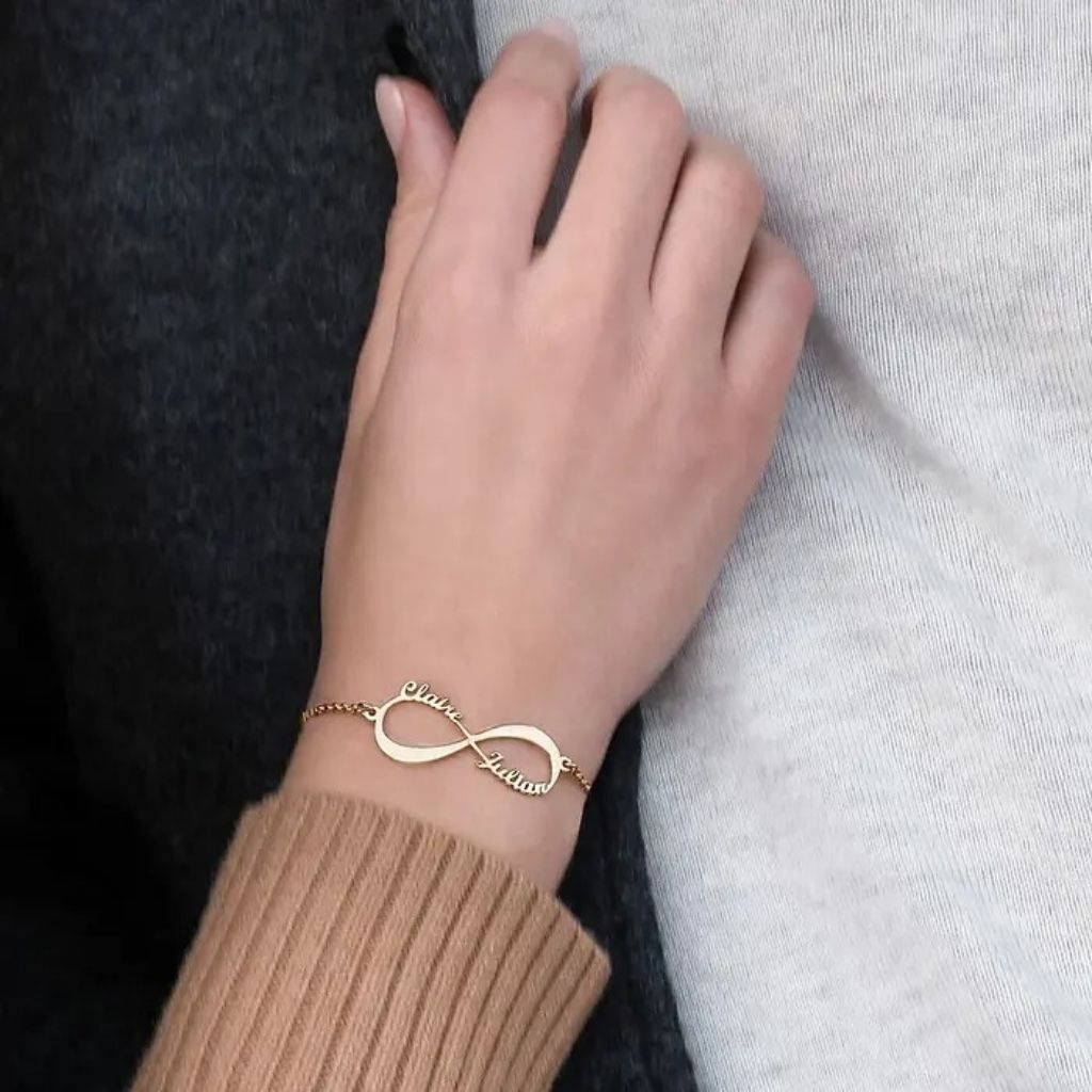 Gold bracelet with infinity symbol on a wrist against a neutral background
