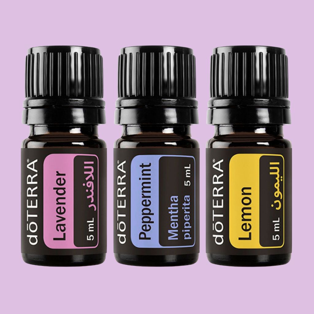 Three doTERRA essential oil bottles labeled Lavender, Peppermint, and Lemon on a purple background.