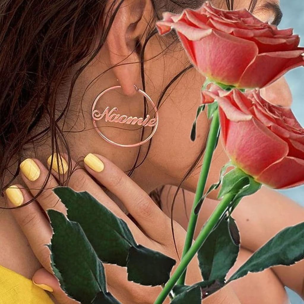 Person wearing a hoop earring with 'Naimie' engraved, holding pink roses.