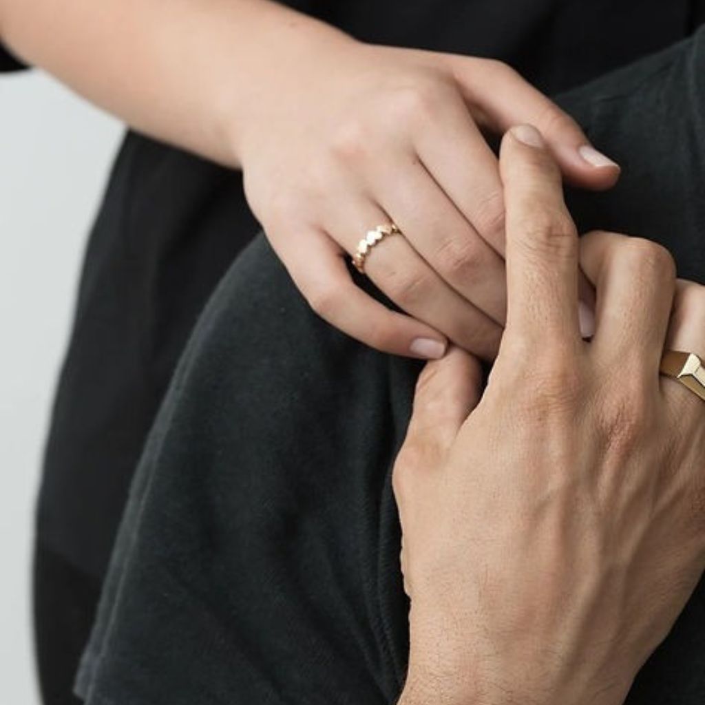 Close-up of two hands holding each other, wearing gold rings.