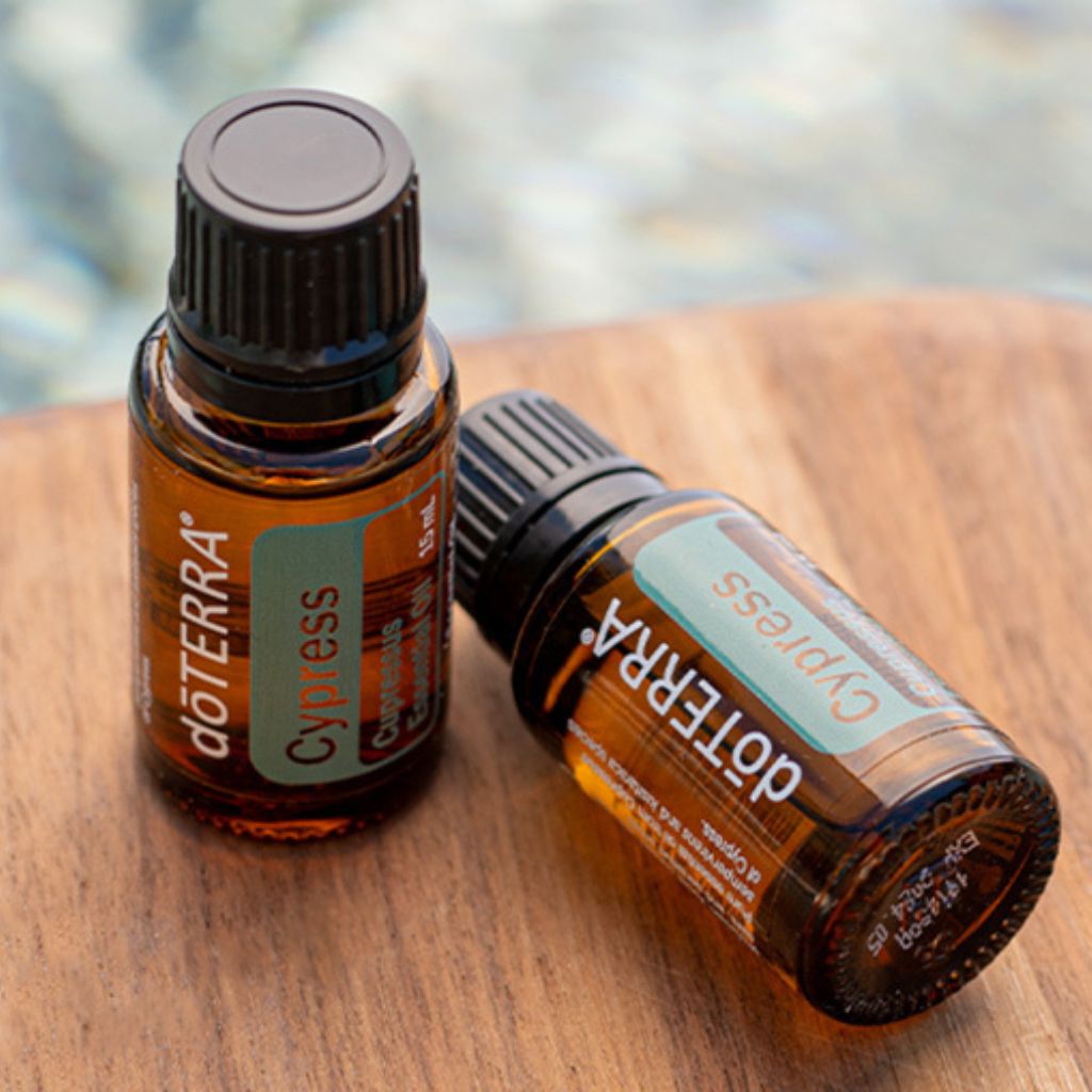 Two doTERRA Cypress essential oil bottles on a wooden surface with a blurred natural background.