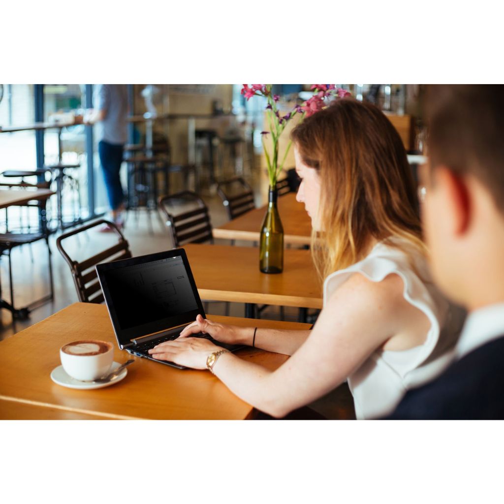 Woman using a laptop at a table in a cafe with a blurred background