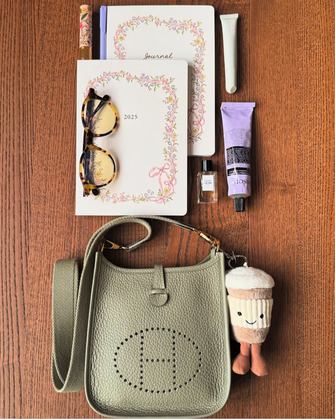 Green handbag with a plush toy, sunglasses, and other items on a wooden surface