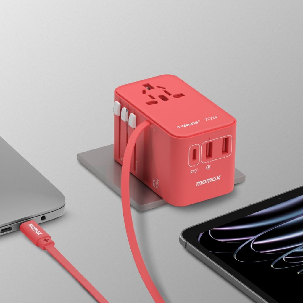 Red power adapter with multiple ports on a gray surface with a laptop and phone.