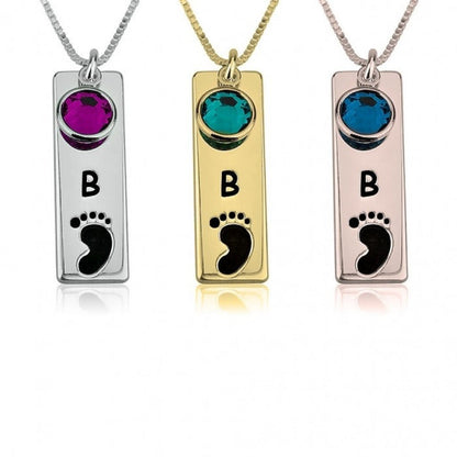 Three necklaces with rectangular pendants featuring initials 'B' and footprints, in silver, gold, and rose gold.