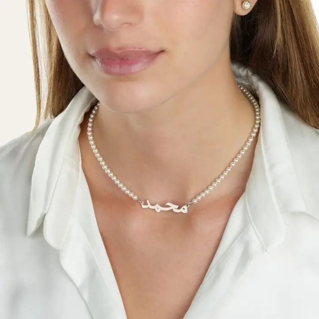 Close-up of a woman wearing a silver necklace with a nameplate against a white background