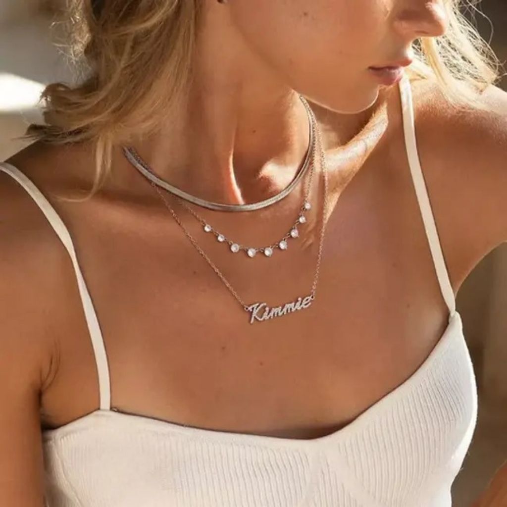 Close-up of a person wearing layered necklaces with 'Kimmie' on a blurred background