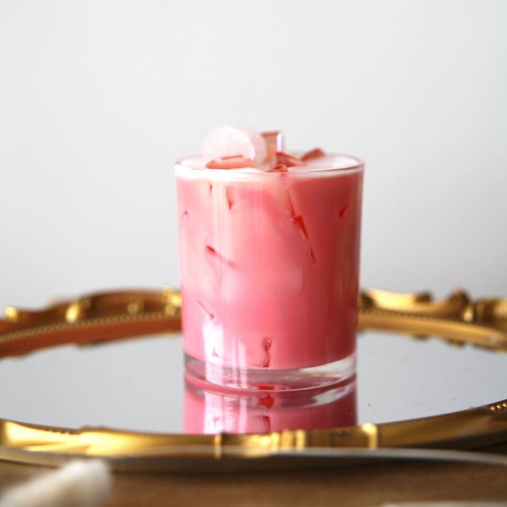 Pink cocktail with ice cubes in a glass on a gold tray against a white background