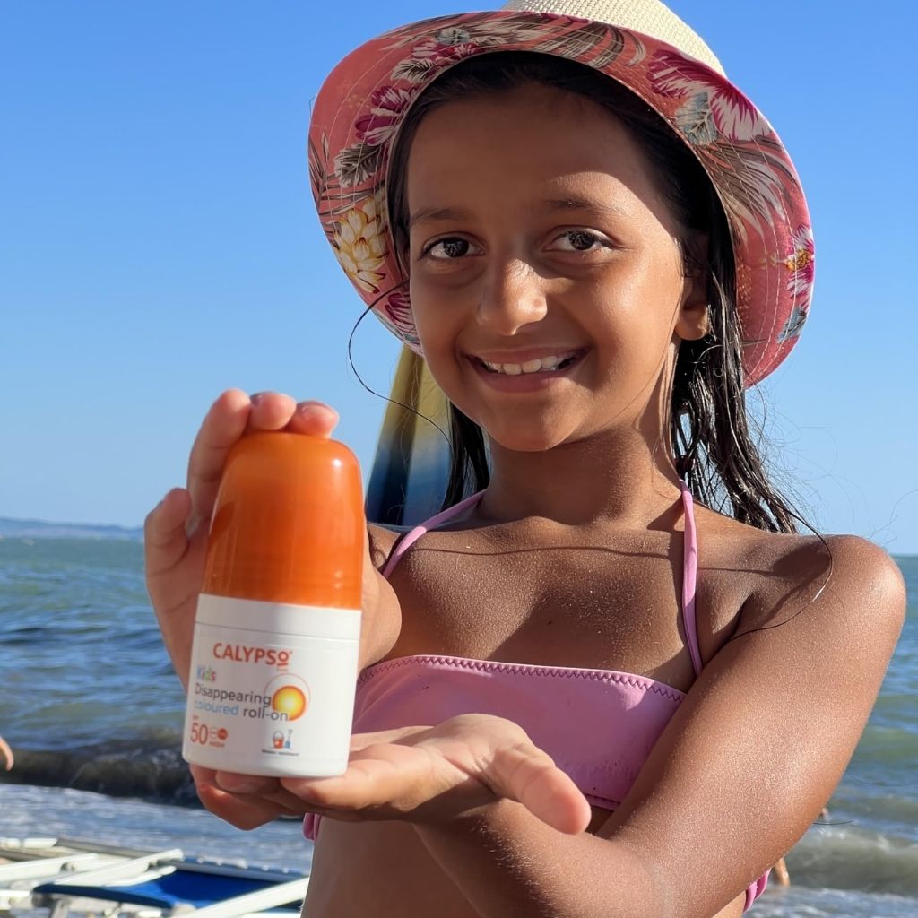 Girl on a beach holding a bottle of Calypso sunscreen