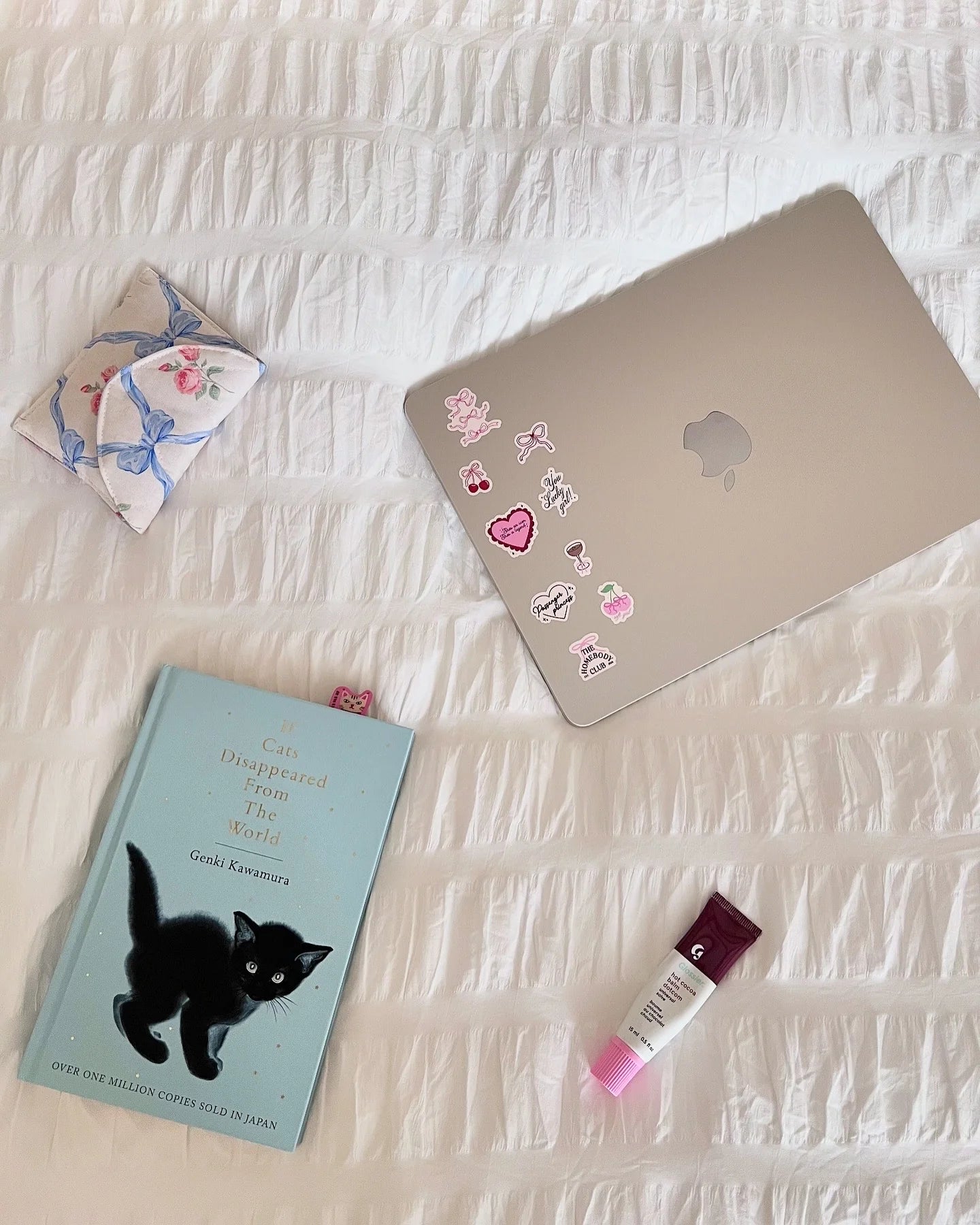 Laptop with stickers, book, and small pouch on a textured surface