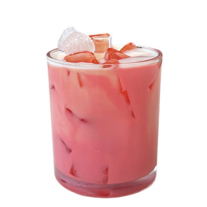 Pink iced drink with fruit pieces in a clear glass on a white background