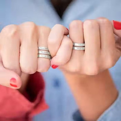 Close-up of two hands wearing silver rings with engraved names.