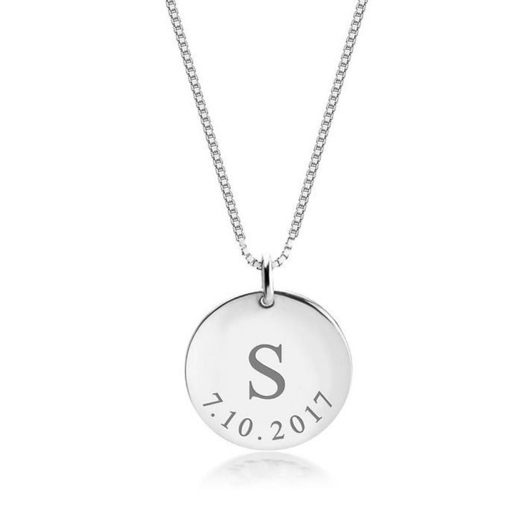 Silver necklace with a round pendant featuring an initial 'S' and date '7.10.2017' on a white background.