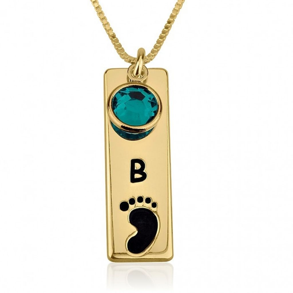 Gold pendant with turquoise gemstone and black footprint design on a white background