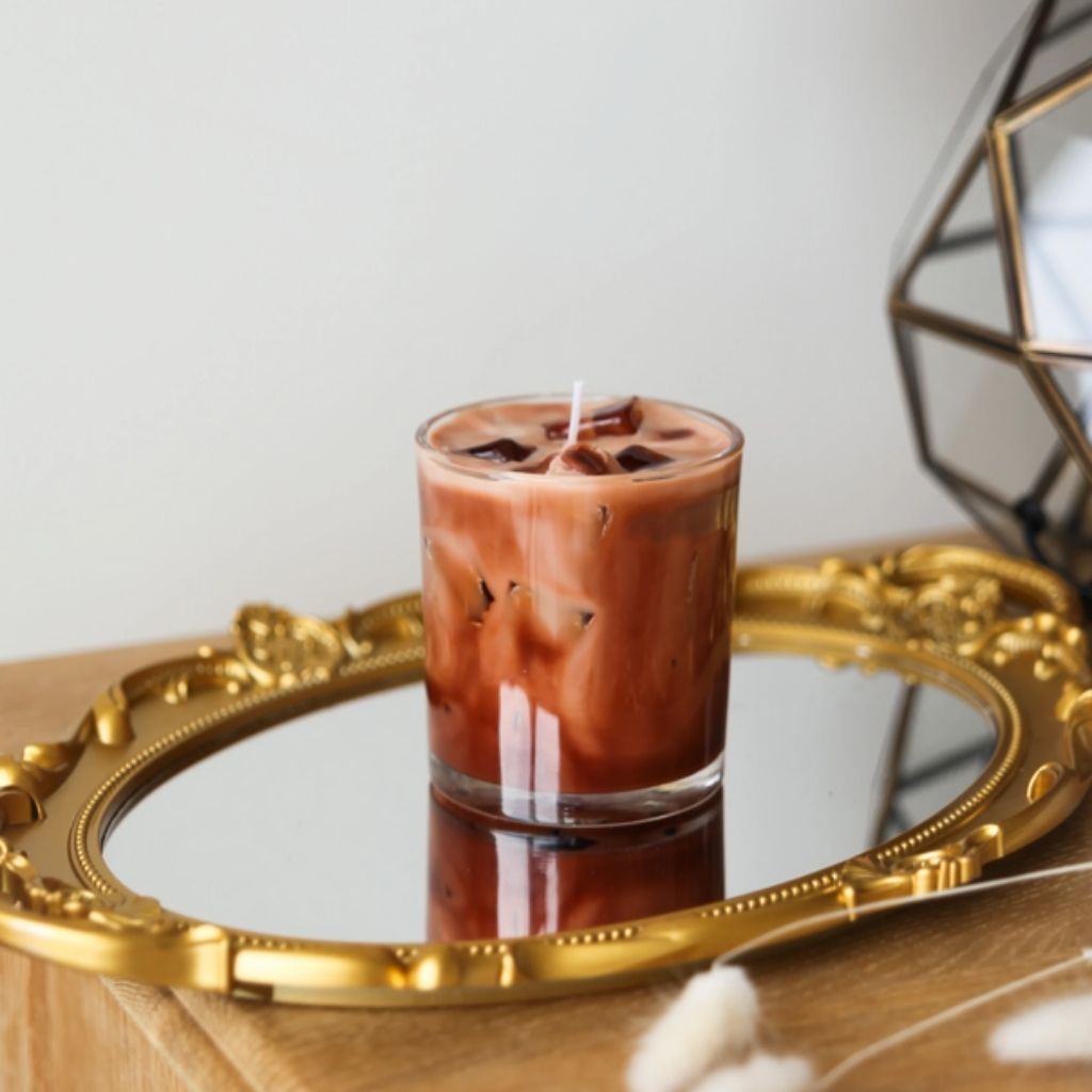 Candle in a glass container on a decorative tray with a geometric mirror in the background