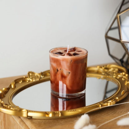 Candle in a glass container on a decorative tray with a geometric mirror in the background