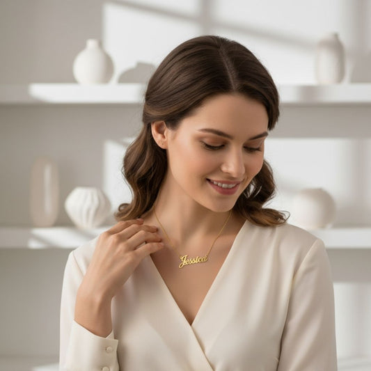 Woman wearing a gold necklace with 'Jessica' engraved, in a softly lit room.
