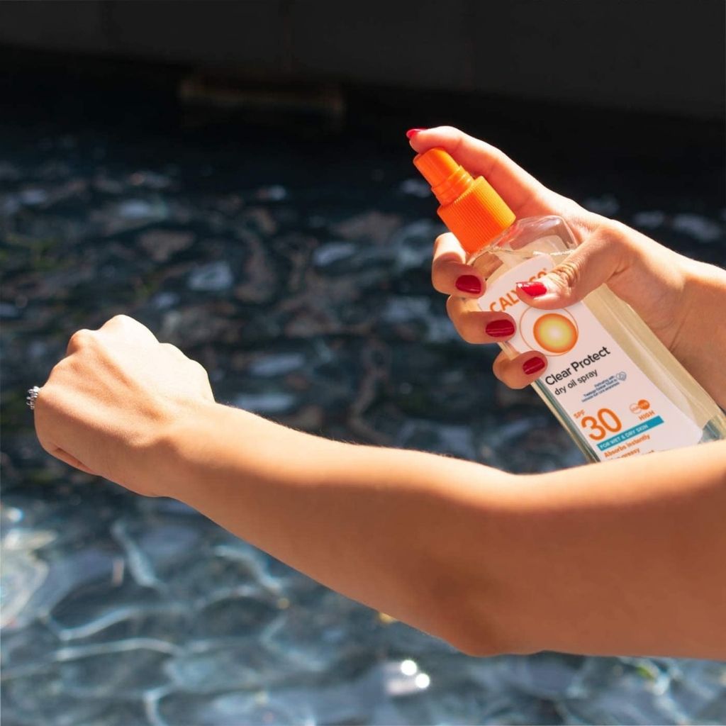 Person applying sunscreen spray to their arm with a blurred background