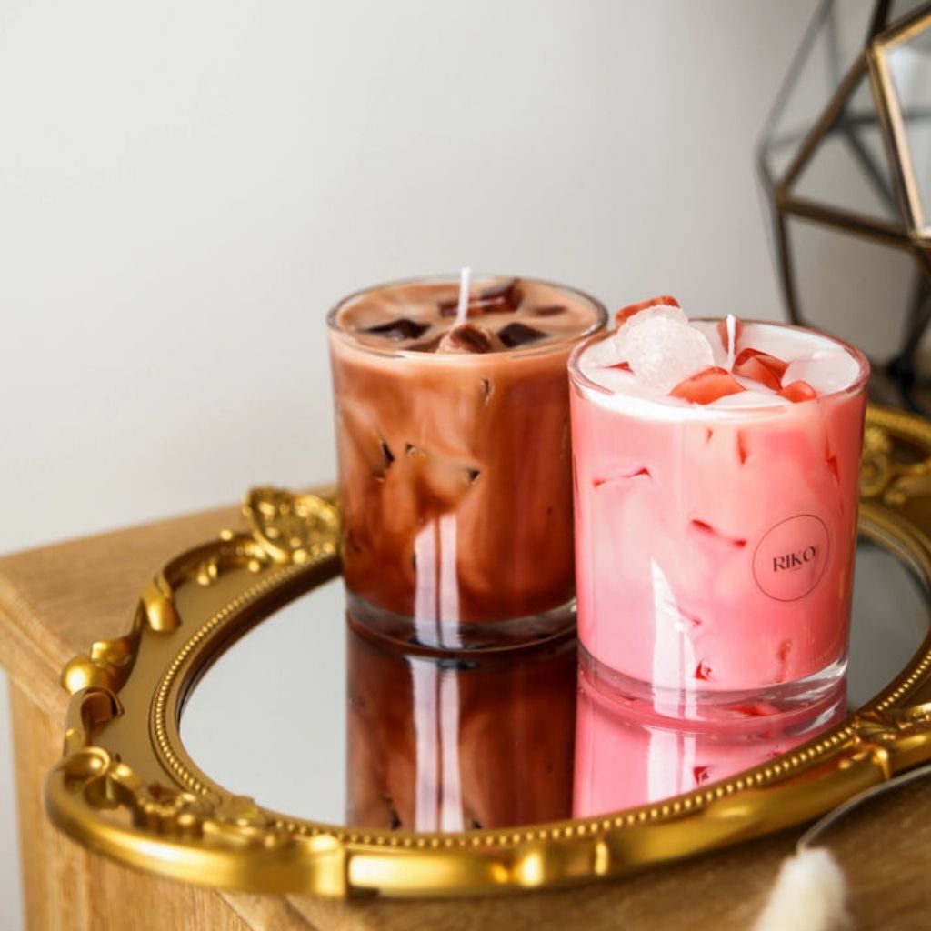 Two candles in glass containers on a gold tray with a white background