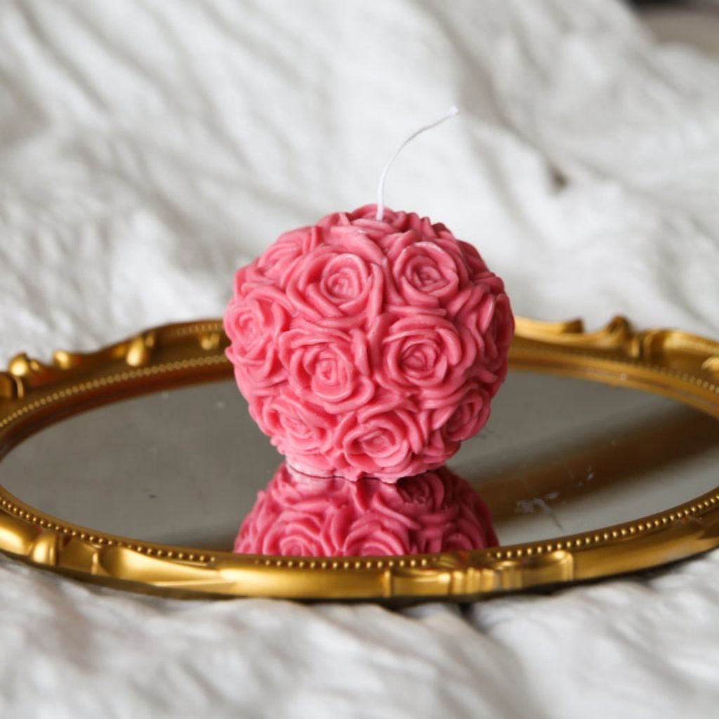Pink rose-patterned candle on a gold mirror with a white textured background