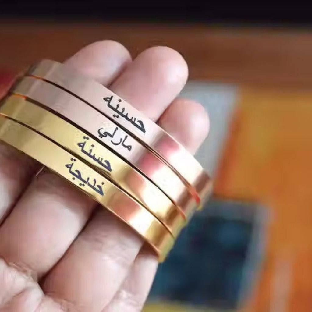 Three gold bracelets with Arabic text on a blurred background