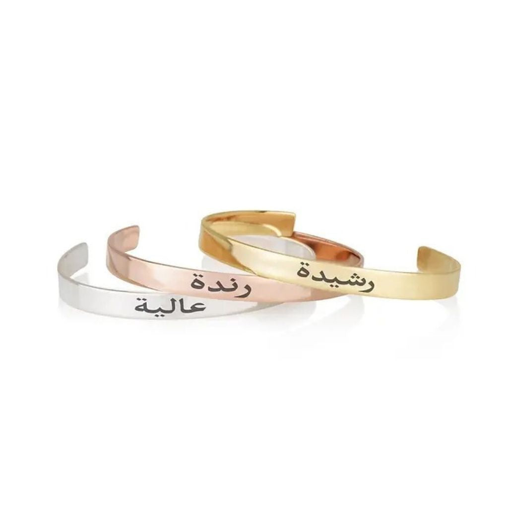 Three gold, silver, and rose gold bangles with Arabic text on a white background