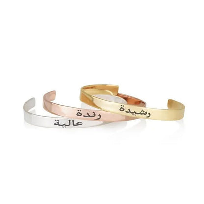 Three gold, silver, and rose gold bangles with Arabic text on a white background