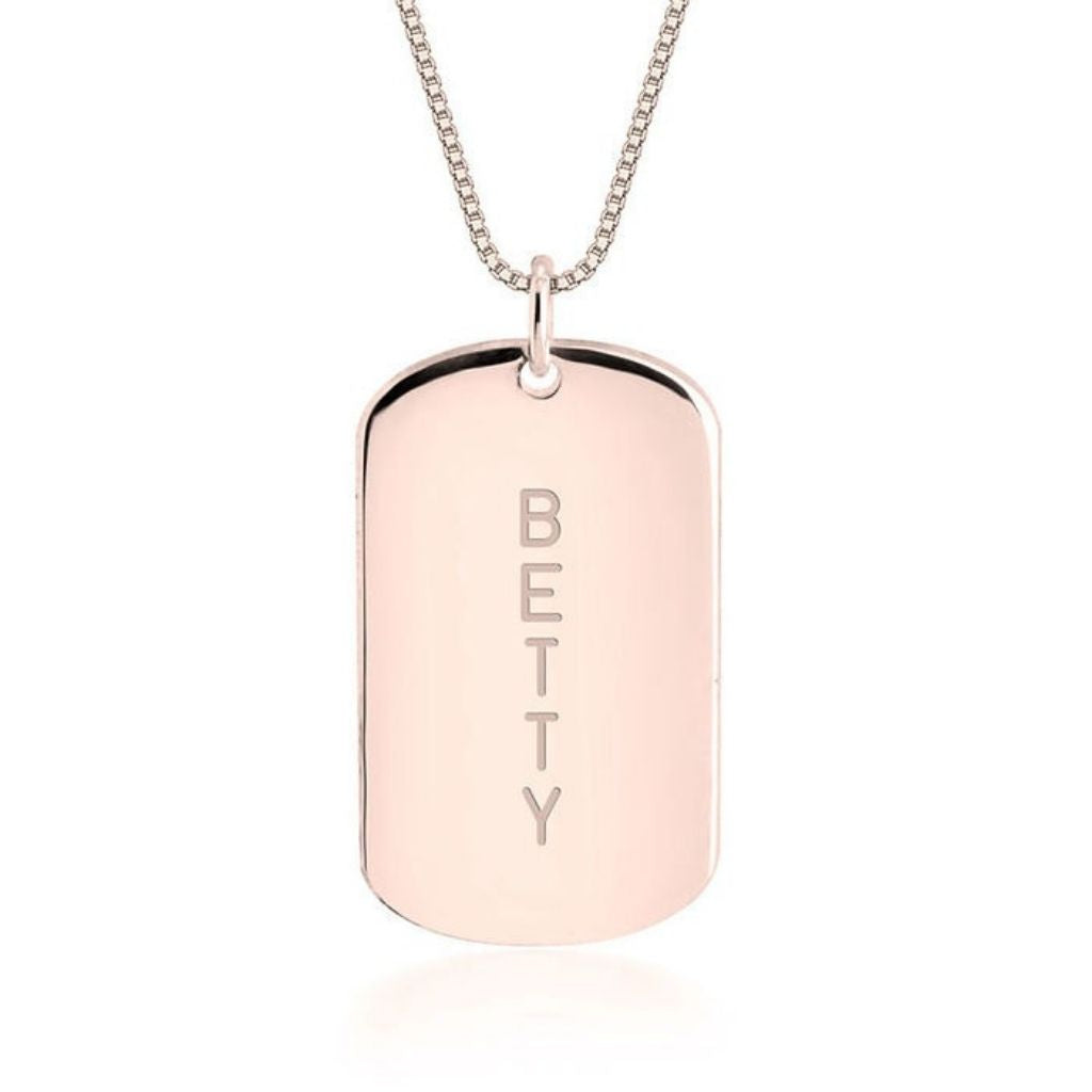 Rose gold dog tag necklace with 'BETTY' engraving on a white background