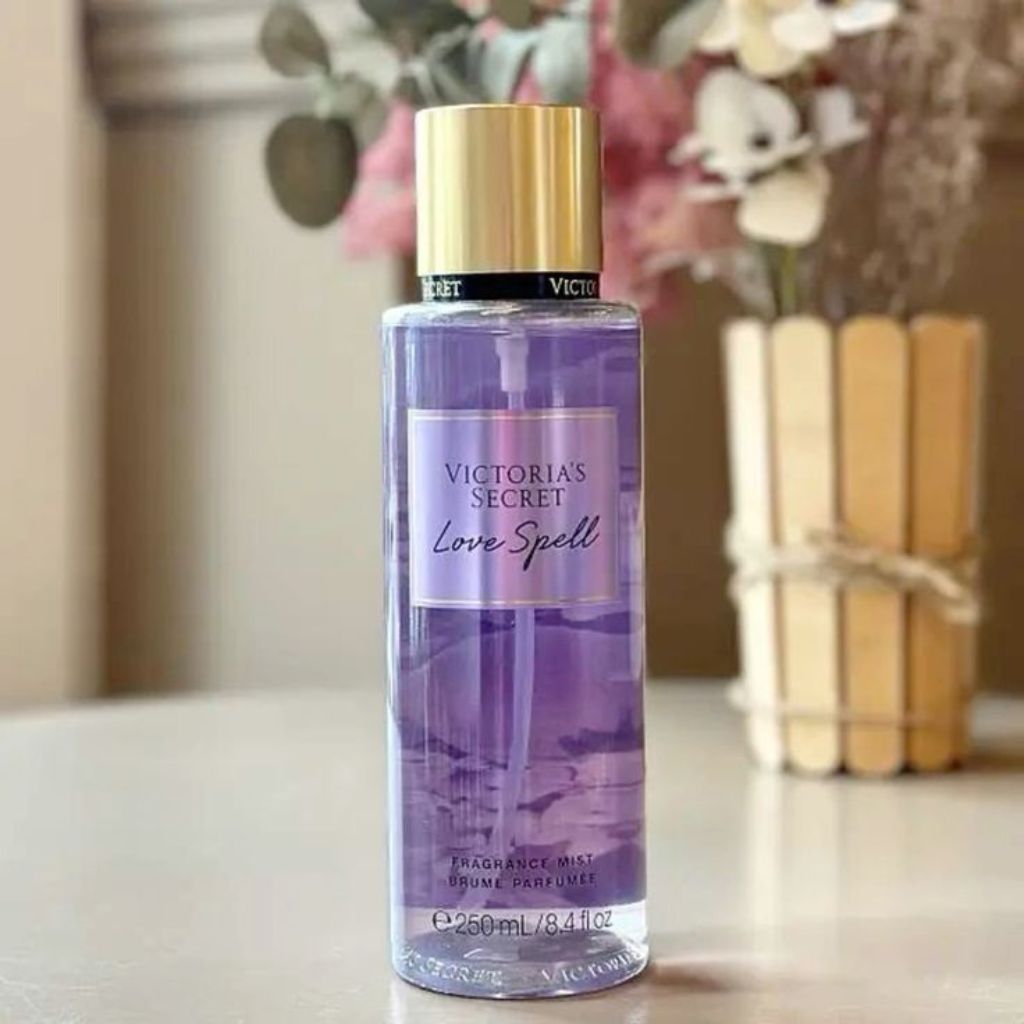 Victoria's Secret Love Spell fragrance mist bottle on a table with flowers in the background