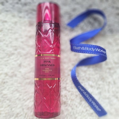 Bath & Body Works Pink Obsessed perfume bottle with a blue ribbon on a textured surface