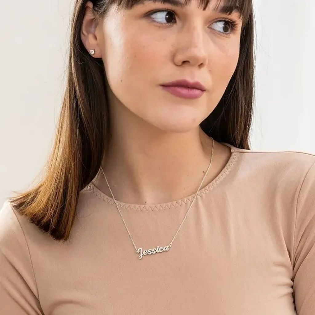 Woman wearing a gold necklace with 'Jessica' engraved on it against a plain background