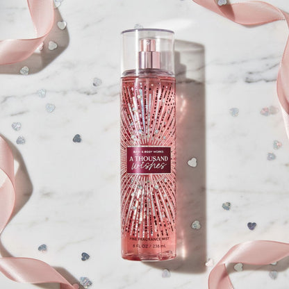 Bath & Body Works 'A Thousand Wishes' perfume spray bottle on a decorative background with ribbons and heart shapes.