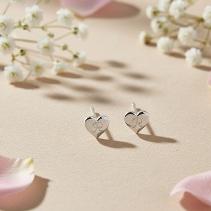 Heart-shaped earrings with initials on a beige surface with flowers
