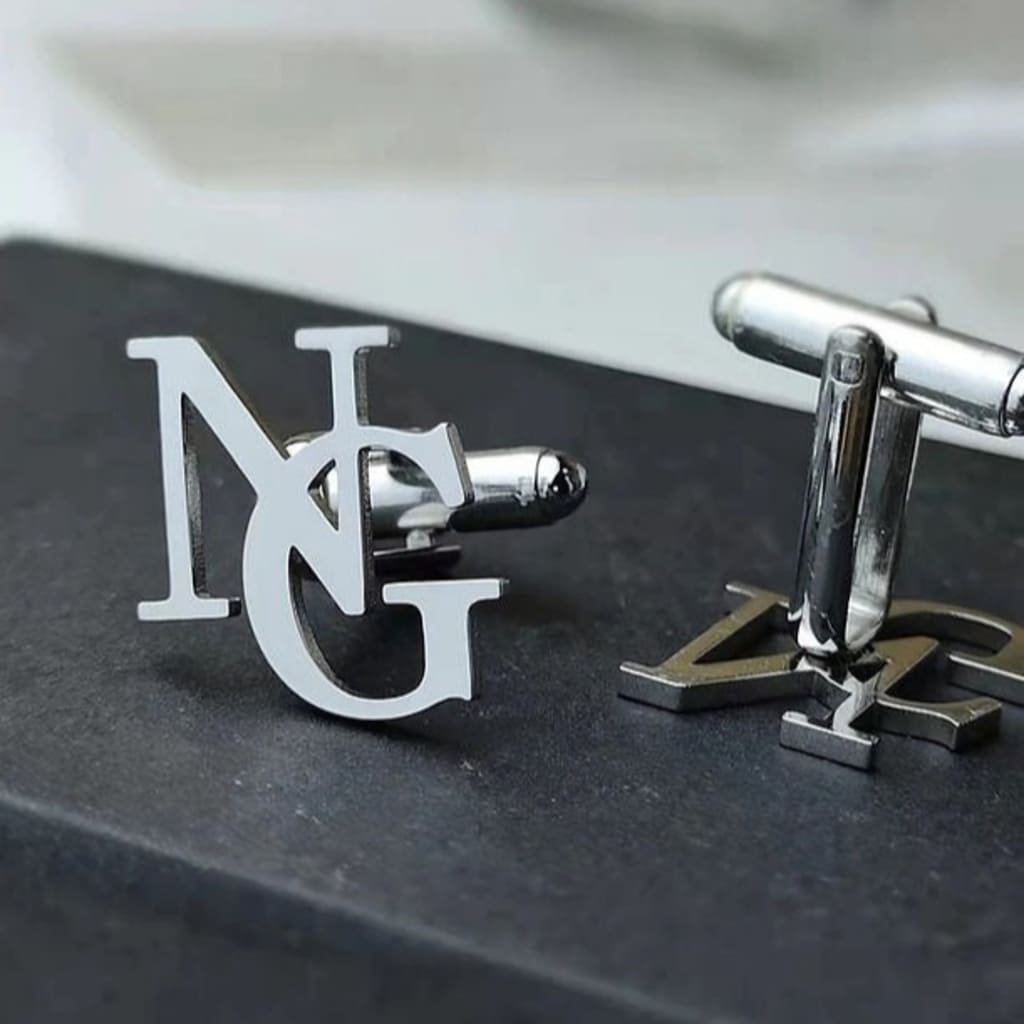 Silver cufflinks with initials on a dark surface