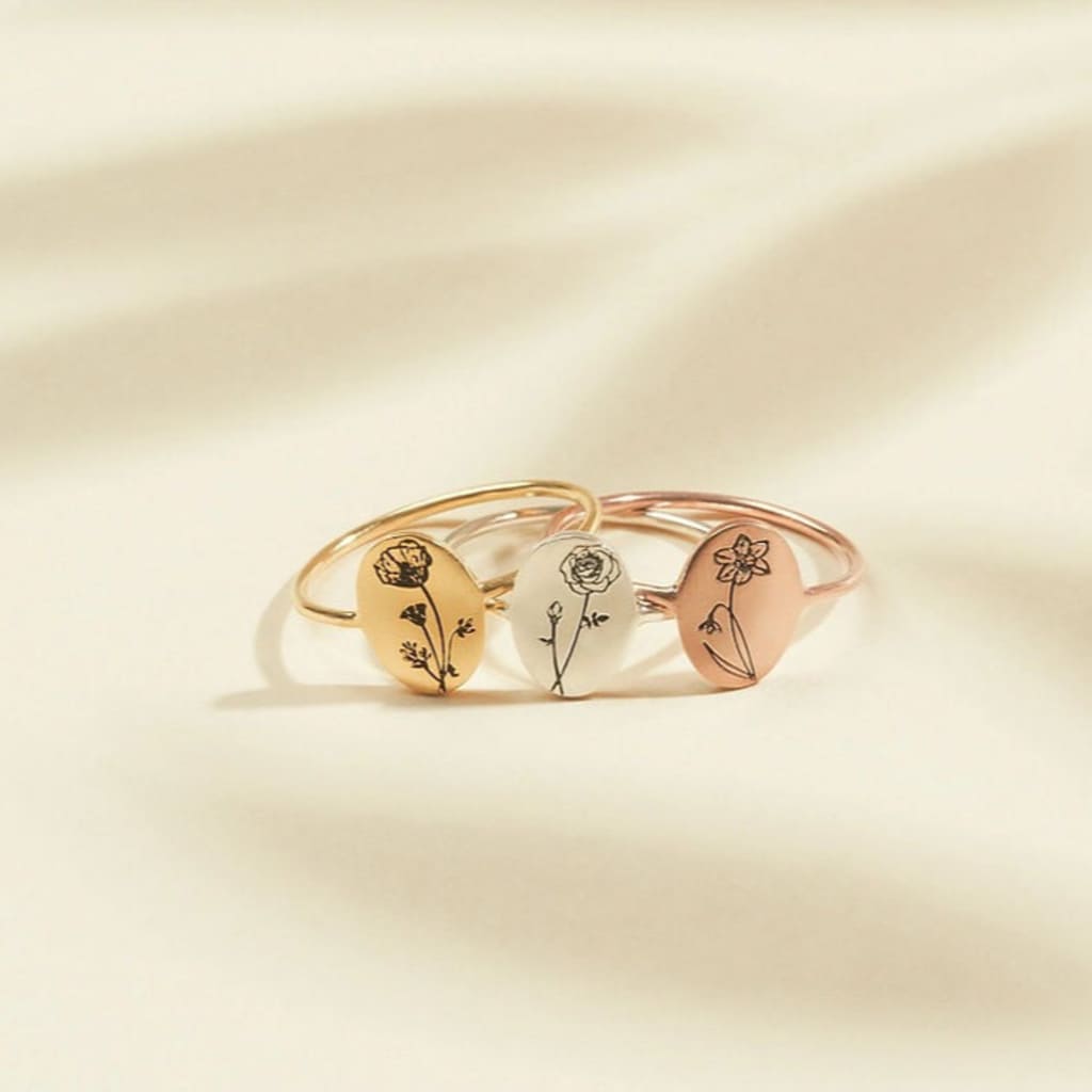 Set of three gold rings with floral designs on a beige background