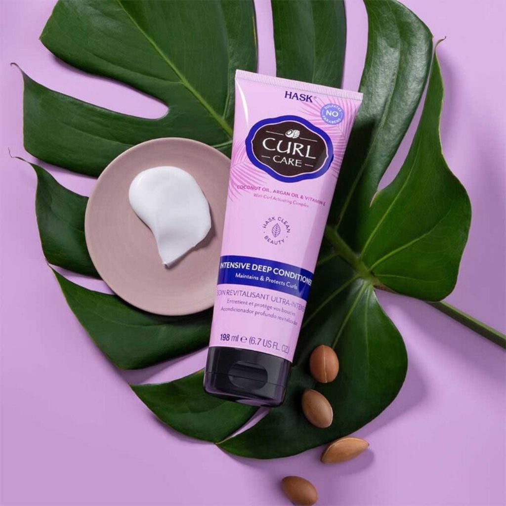 Tube of HASK Curl and Cake Deep Conditioner on a purple background with leaves and almonds.