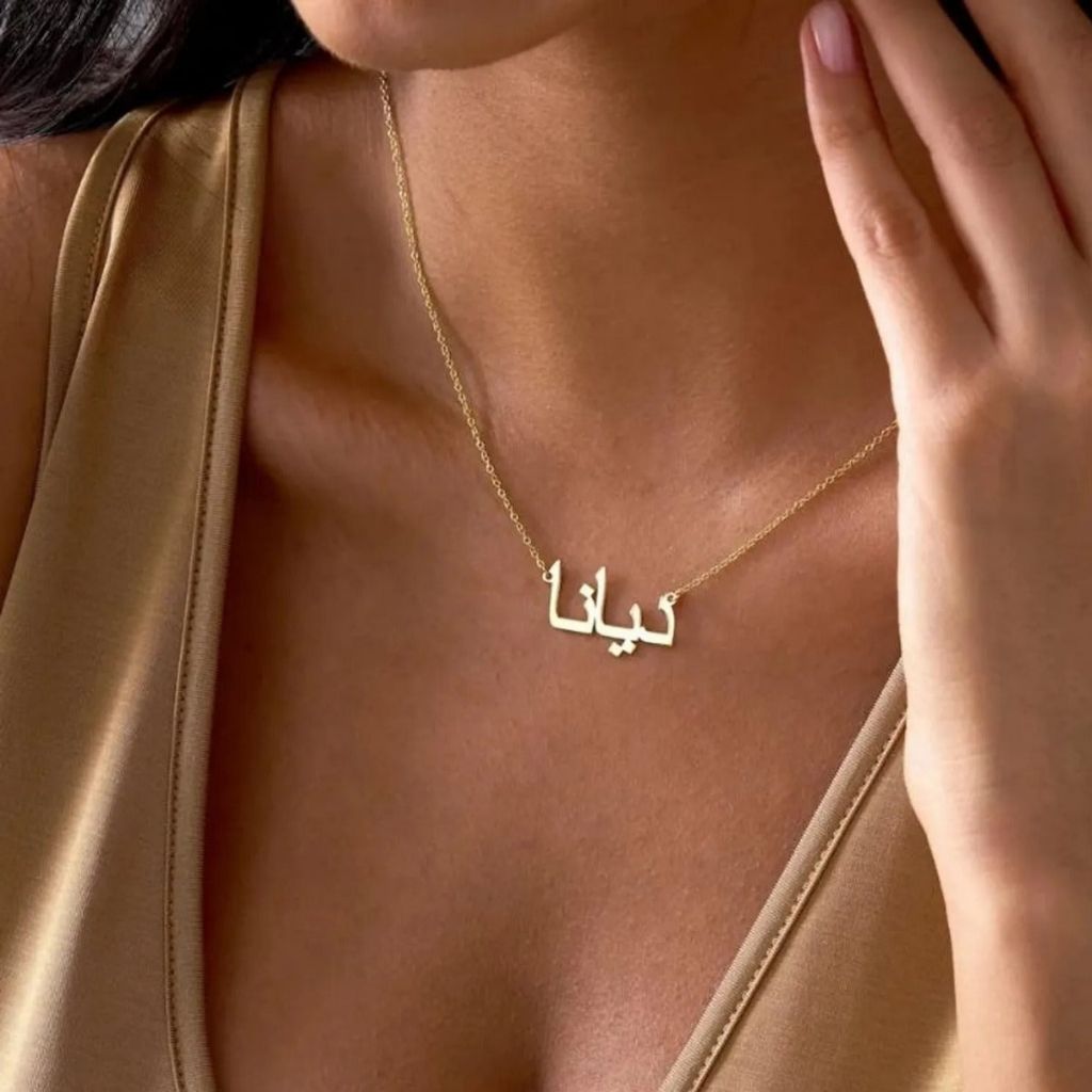 Gold necklace with Arabic script worn by a person in a gold dress.