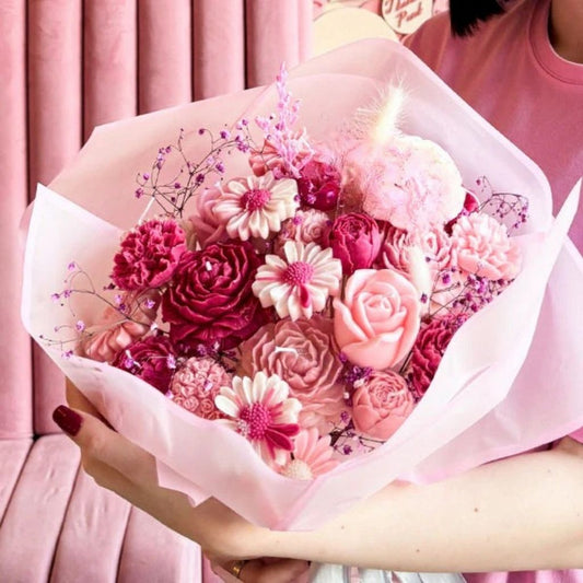 Bouquet of pink flowers held by a person against a pink background
