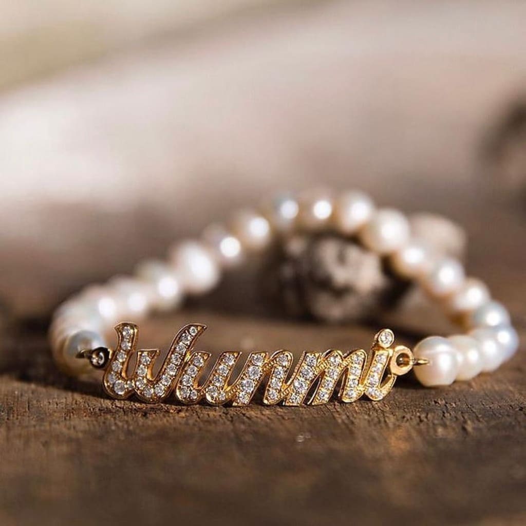 Pearl bracelet with a gold charm displaying 'Wunmi' on a wooden surface.