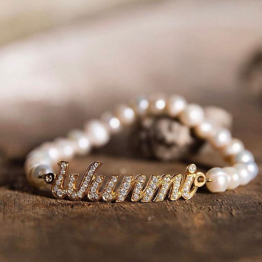 Pearl bracelet with a gold charm displaying 'Wunmi' on a wooden surface.