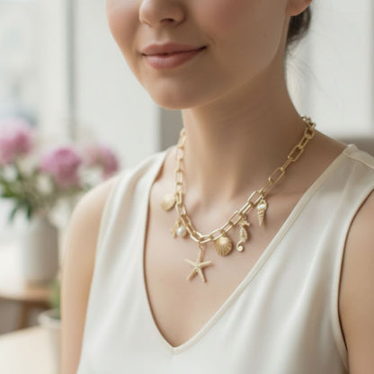 Woman wearing a gold necklace with shell and starfish charms in a softly blurred indoor setting.