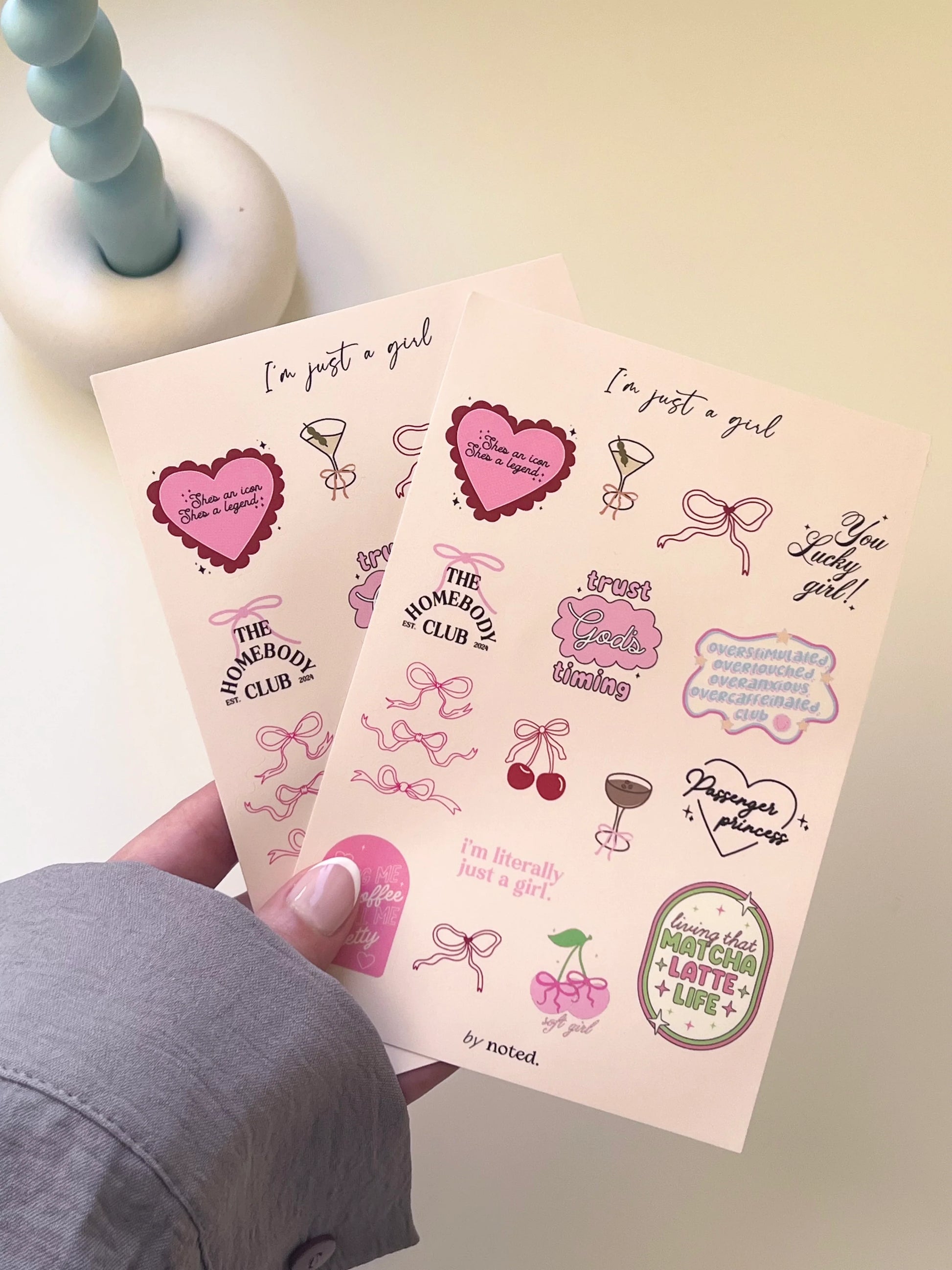 Two sheets of pink stickers with various designs and text held by a person.
