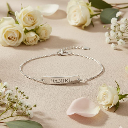 Silver bracelet with engraved name 'DANIEL' on a beige surface with white roses.