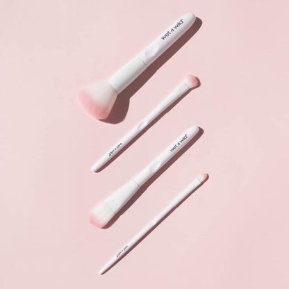 Three makeup brushes with pink bristles and white handles on a pink background, branded 'Wet n Wild'.