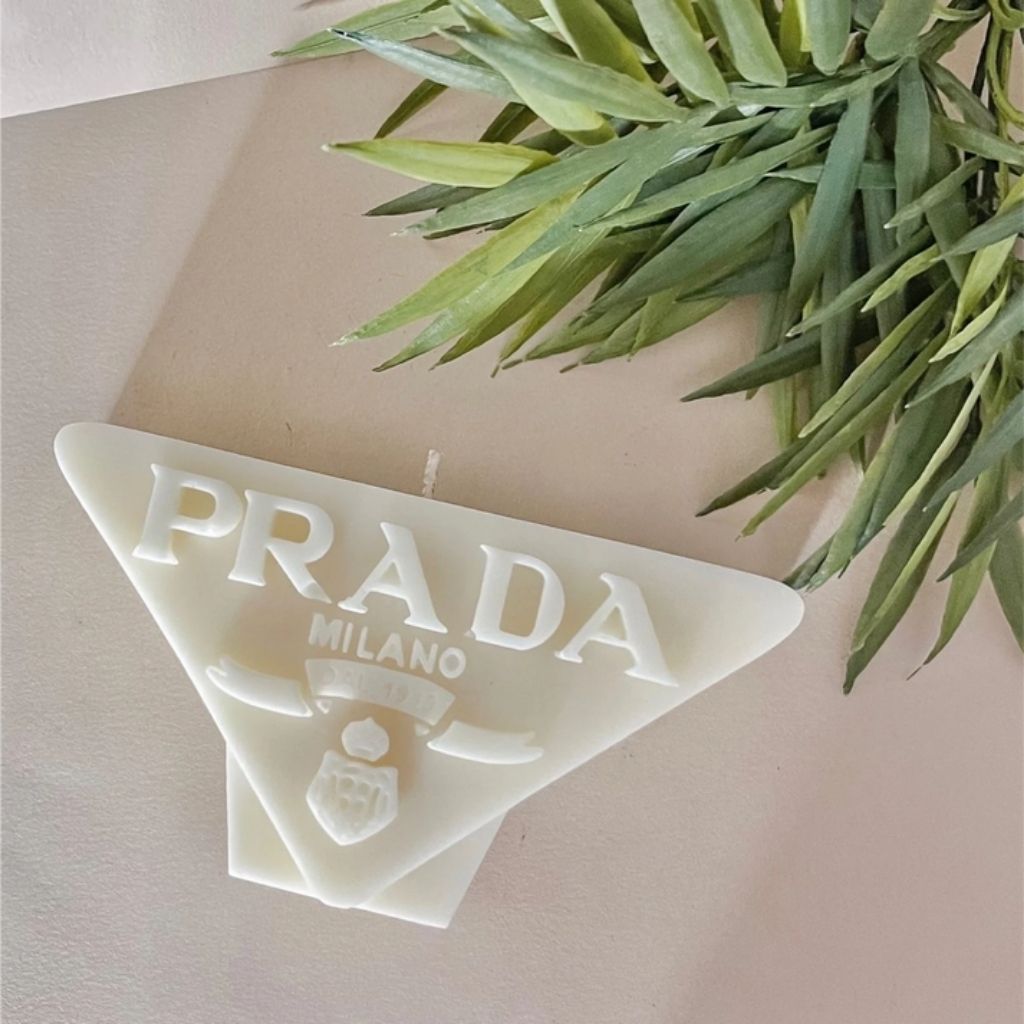 Triangular Prada Milano soap on a beige background with green leaves.