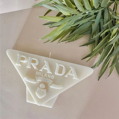 Triangular Prada Milano soap on a beige background with green leaves.